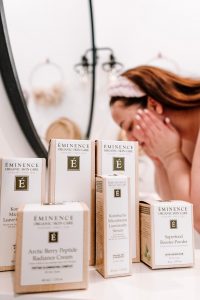 girl washing face in background with Eminence Organic Skin Care products shown in front